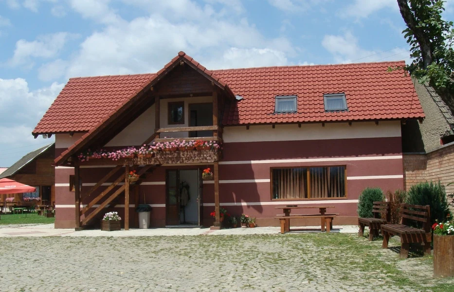 Casa La Moara, cu balcon din lemn, flori și acoperiș de țiglă